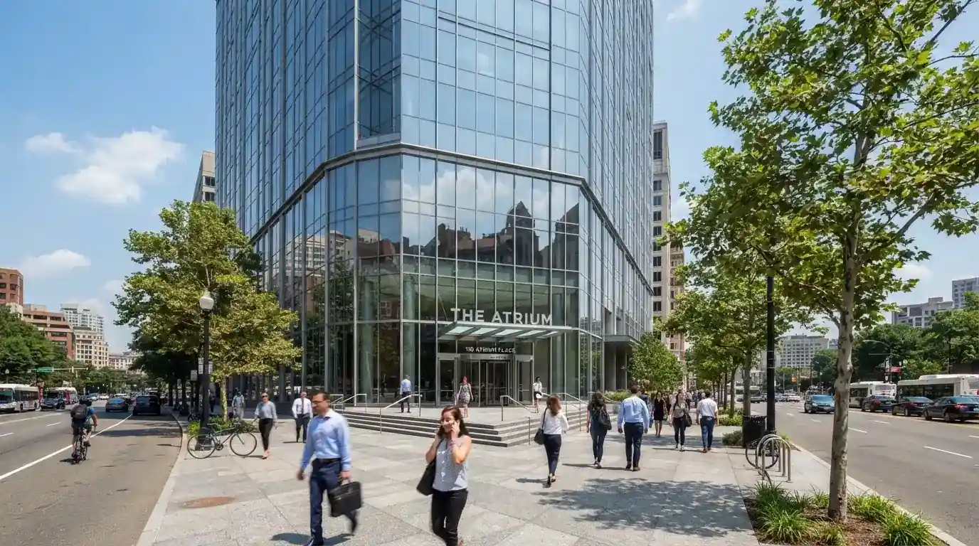 Edificio de oficinas moderno con fachada de cristal bajo un cielo despejado, gente caminando por la acera en una calle de ciudad.
