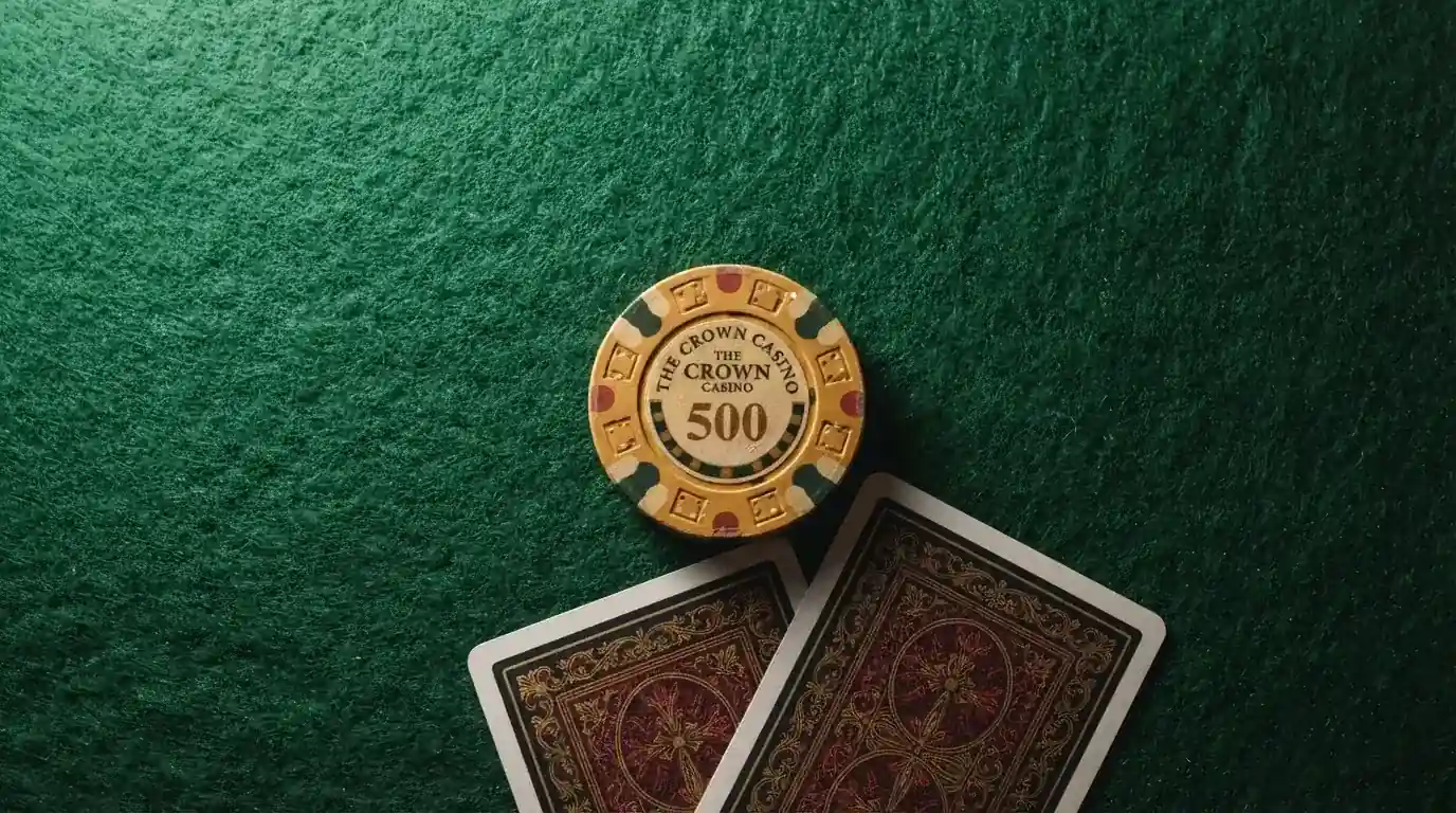 Vista cenital de fichas doradas y una baraja de cartas sobre una mesa de fieltro verde.